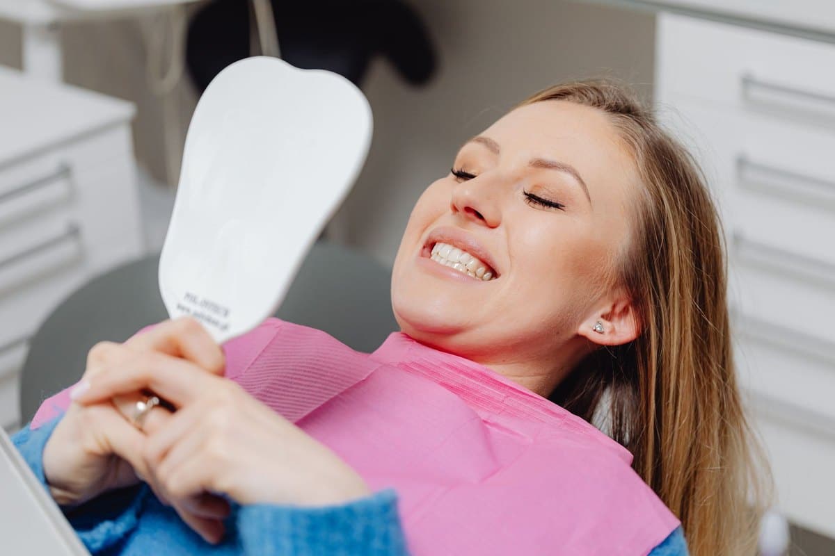 Mujer sonriendo con un espejo en una clínica dental